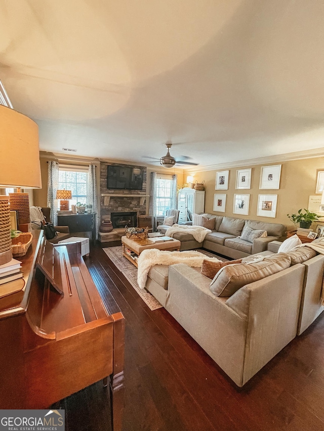 living area with a ceiling fan, plenty of natural light, dark wood finished floors, and a stone fireplace