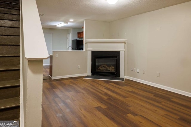 unfurnished living room featuring dark wood-style floors, stairs, baseboards, and a textured ceiling