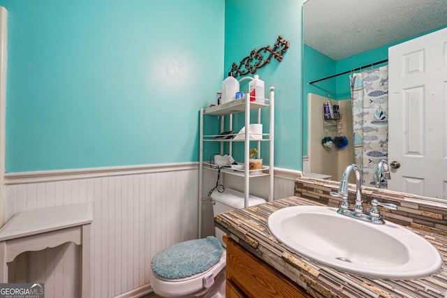 bathroom featuring wainscoting, toilet, curtained shower, a textured ceiling, and vanity