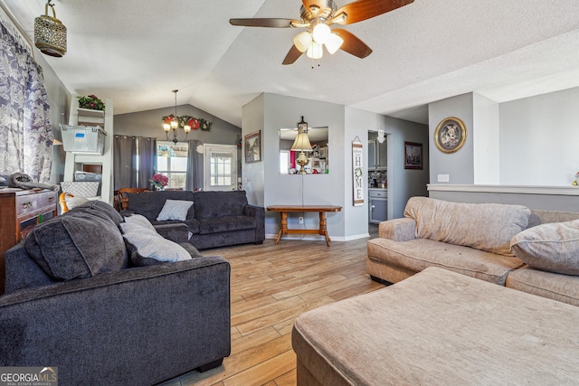 living room featuring lofted ceiling, a textured ceiling, light wood-type flooring, baseboards, and ceiling fan with notable chandelier