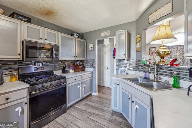 kitchen featuring stainless steel appliances, light countertops, wood tiled floor, a sink, and a textured ceiling