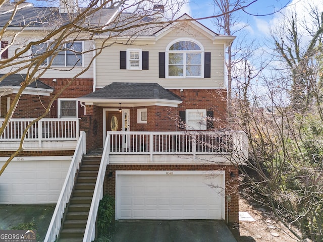 townhome / multi-family property with stairway, driveway, roof with shingles, a garage, and brick siding