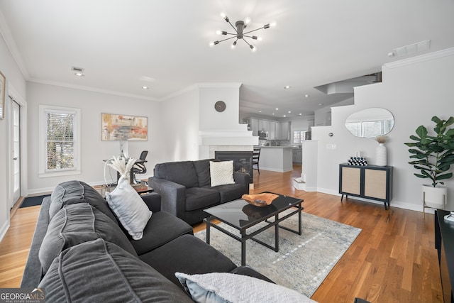 living area with baseboards, an inviting chandelier, light wood-style flooring, recessed lighting, and ornamental molding