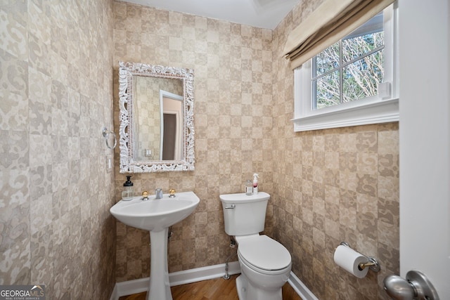 half bath with toilet, baseboards, and wood finished floors