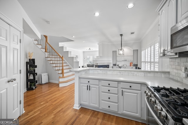 kitchen featuring light wood-type flooring, backsplash, appliances with stainless steel finishes, a peninsula, and light countertops