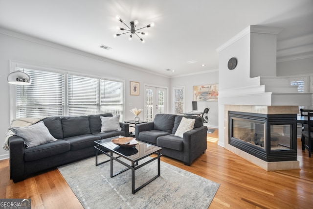 living area with visible vents, wood finished floors, crown molding, and a tile fireplace