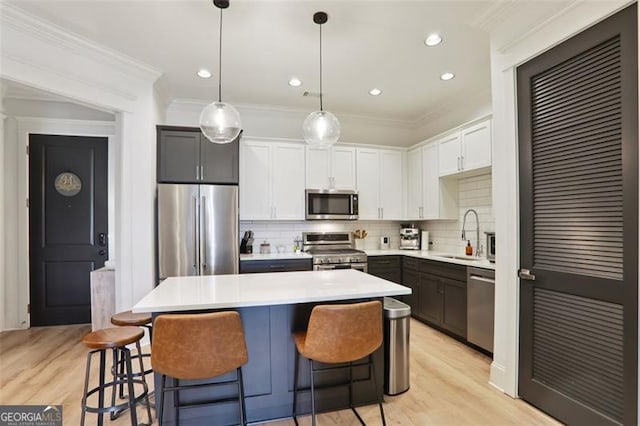 kitchen with a sink, white cabinets, light countertops, appliances with stainless steel finishes, and crown molding