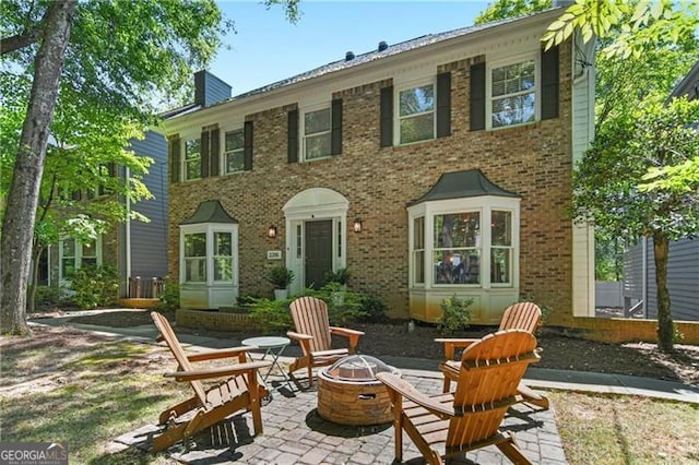 back of property with an outdoor fire pit, a chimney, a patio area, and brick siding