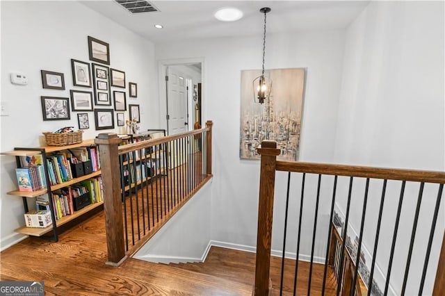 hall featuring baseboards, visible vents, wood finished floors, and an upstairs landing