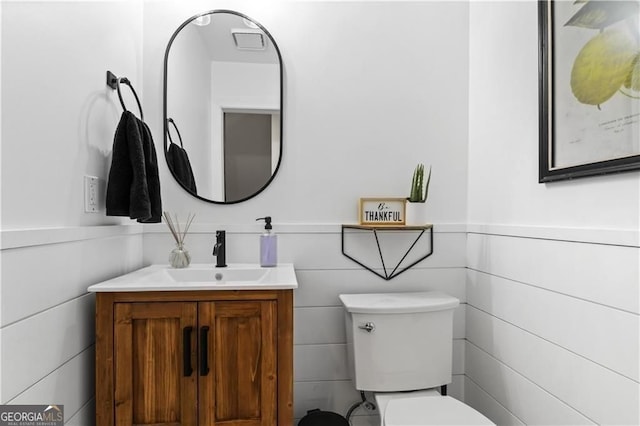 half bathroom with tile walls, wainscoting, vanity, and toilet