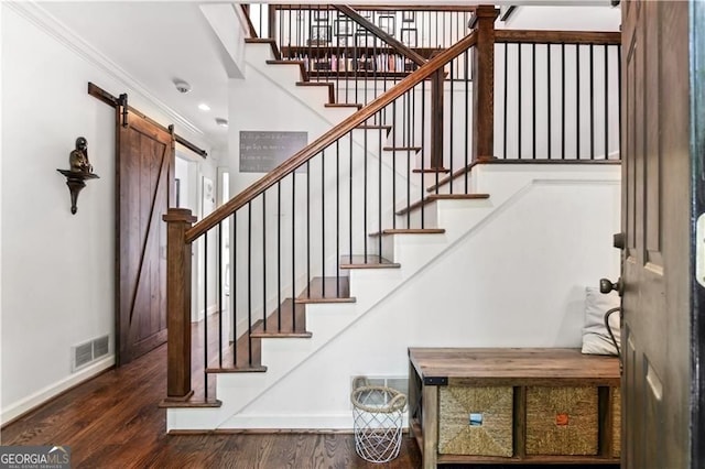 stairs with a barn door, wood finished floors, visible vents, and baseboards