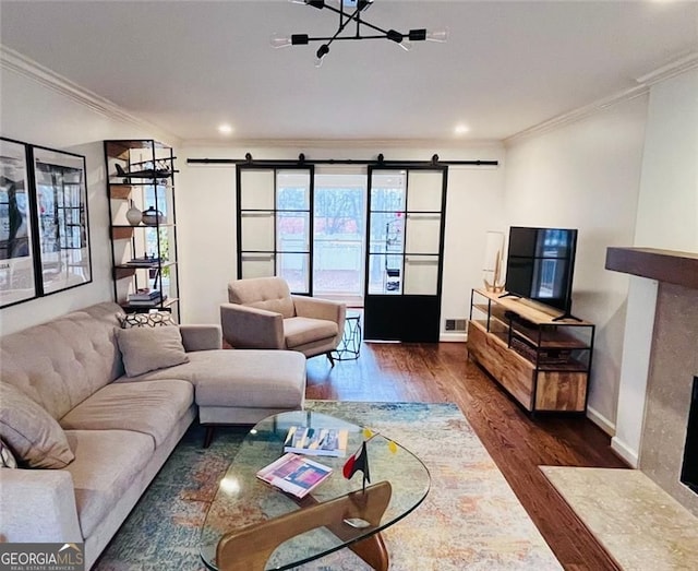 living room with a barn door, baseboards, ornamental molding, wood finished floors, and a fireplace