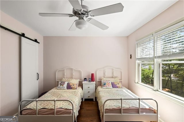 bedroom with ceiling fan, a barn door, and dark wood-type flooring