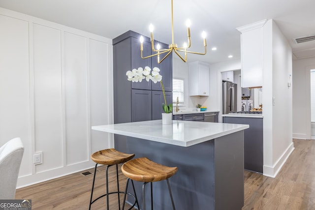 kitchen featuring light wood-type flooring, stainless steel fridge, visible vents, and a breakfast bar area