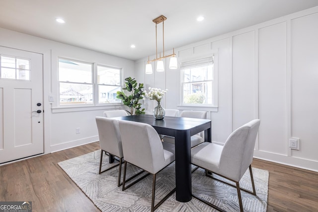 dining area featuring baseboards, a decorative wall, wood finished floors, and recessed lighting