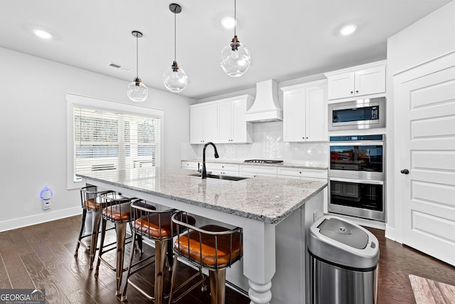 kitchen with dark wood-style flooring, stainless steel appliances, tasteful backsplash, a sink, and premium range hood