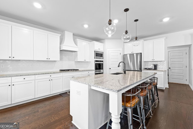 kitchen featuring a center island with sink, appliances with stainless steel finishes, dark wood-type flooring, a sink, and premium range hood