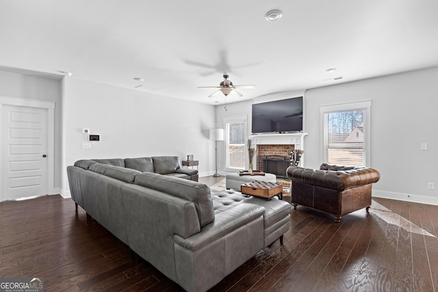 living room featuring a ceiling fan, a brick fireplace, dark wood-style flooring, and baseboards