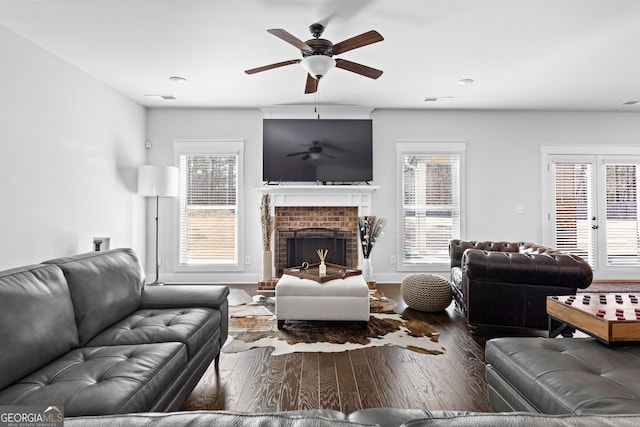 living room with wood finished floors, visible vents, baseboards, a ceiling fan, and a brick fireplace