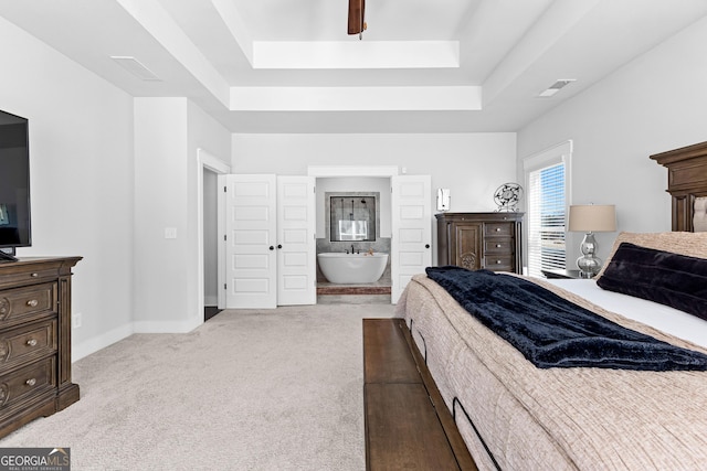 carpeted bedroom featuring ensuite bath, visible vents, a tray ceiling, and baseboards