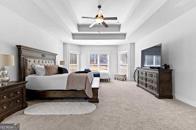 carpeted bedroom with ceiling fan, a raised ceiling, visible vents, and baseboards