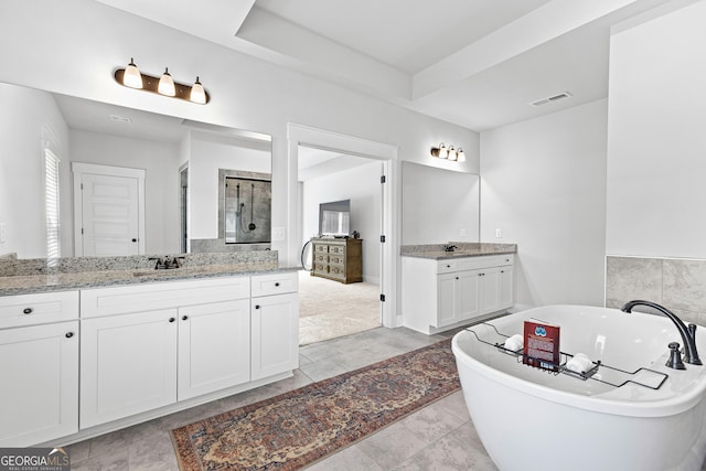 full bath featuring visible vents, two vanities, a freestanding tub, a shower stall, and a sink