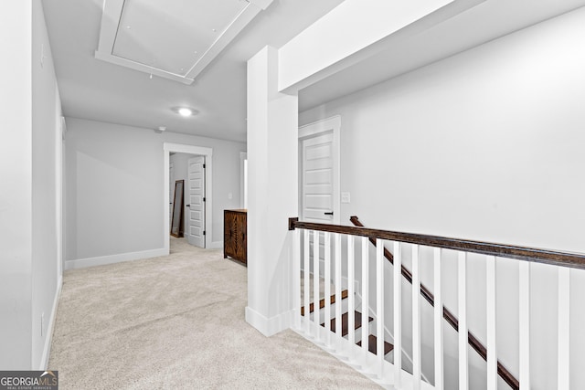 hallway featuring attic access, carpet, baseboards, and an upstairs landing