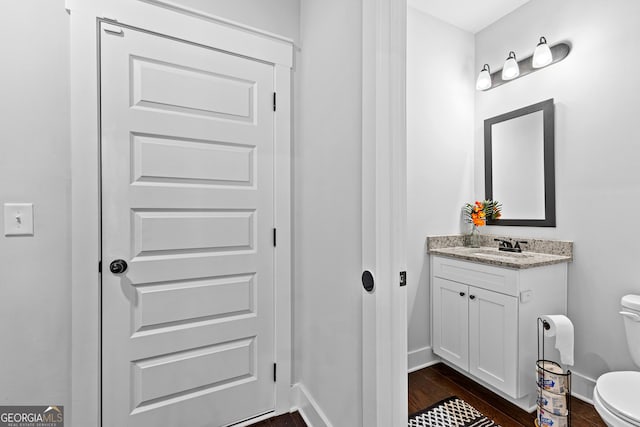 bathroom with toilet, baseboards, wood finished floors, and vanity