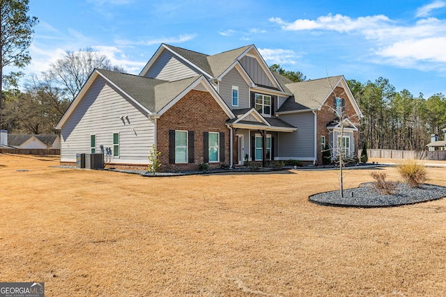 view of front of house with brick siding, a shingled roof, board and batten siding, central AC, and a front lawn