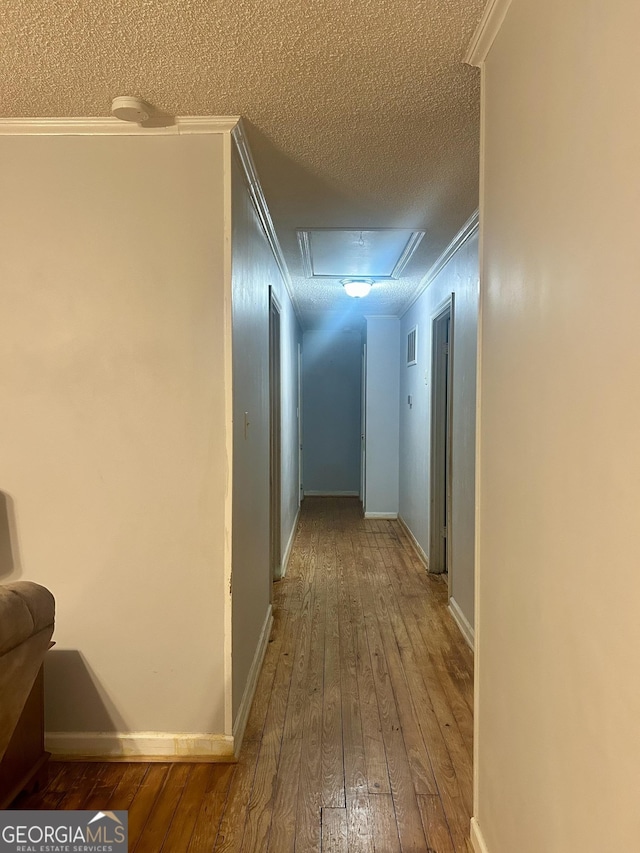 hall featuring a textured ceiling, hardwood / wood-style flooring, visible vents, baseboards, and crown molding