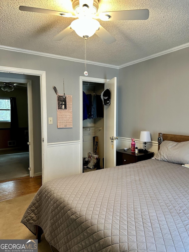 bedroom featuring visible vents, a ceiling fan, ornamental molding, wood finished floors, and a textured ceiling