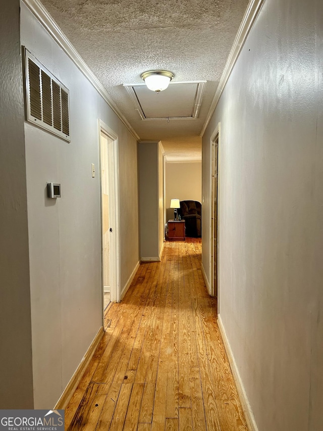 hall with a textured ceiling, light wood finished floors, visible vents, and crown molding