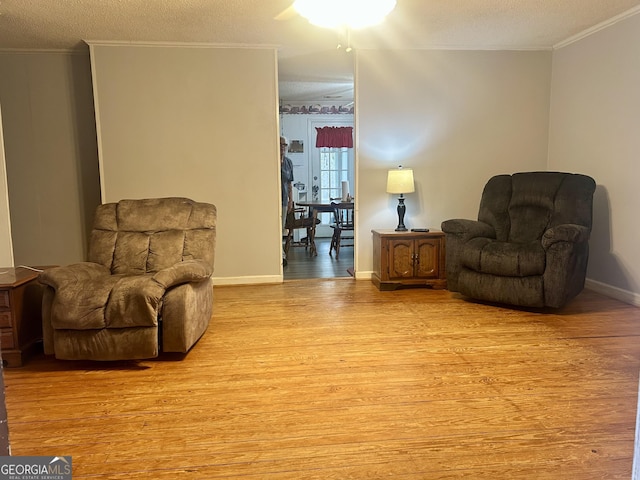 living area with baseboards, ornamental molding, a textured ceiling, and light wood-style floors