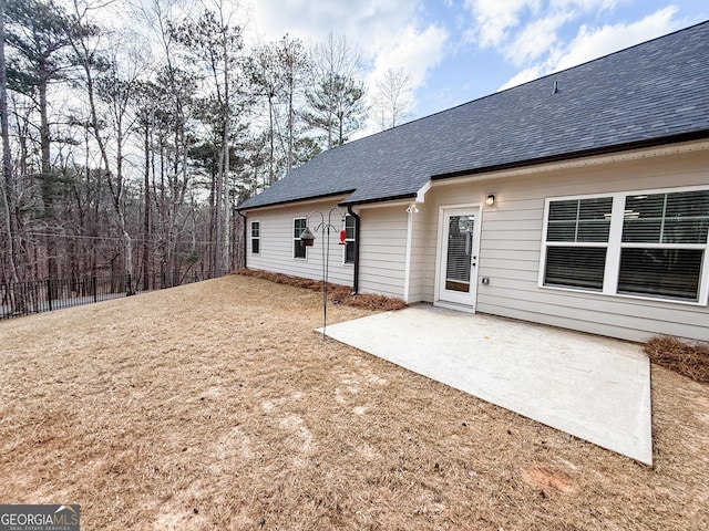 rear view of house featuring a shingled roof, fence, and a patio