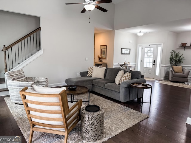 living area featuring a towering ceiling, ceiling fan, stairway, and dark wood-type flooring