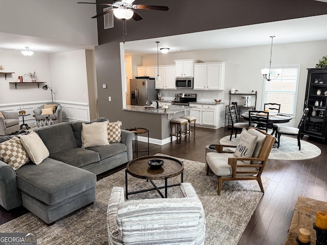 living room featuring dark wood-style floors, a wainscoted wall, and ceiling fan with notable chandelier