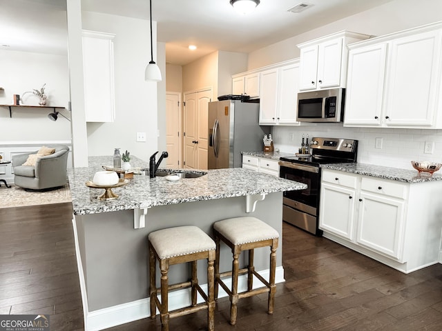 kitchen featuring dark wood-style flooring, appliances with stainless steel finishes, white cabinetry, a sink, and a kitchen breakfast bar