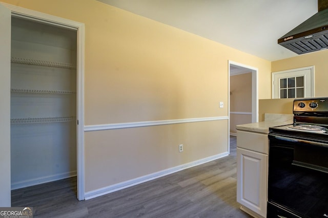 kitchen featuring extractor fan, wood finished floors, white cabinetry, baseboards, and black electric range