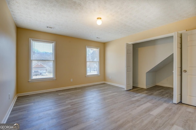 unfurnished bedroom with a textured ceiling, multiple windows, and wood finished floors