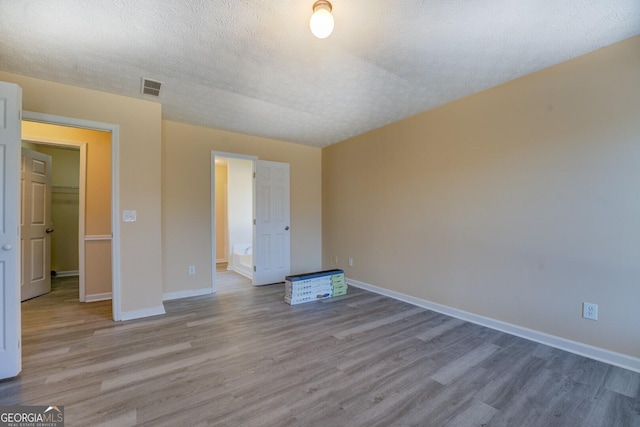 unfurnished room with visible vents, a textured ceiling, baseboards, and wood finished floors