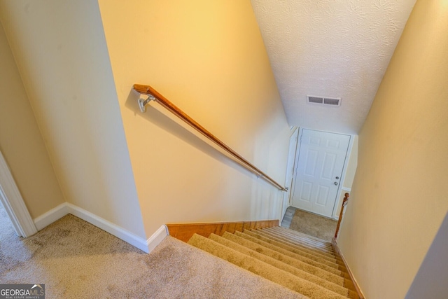 stairs with carpet, visible vents, a textured ceiling, and baseboards