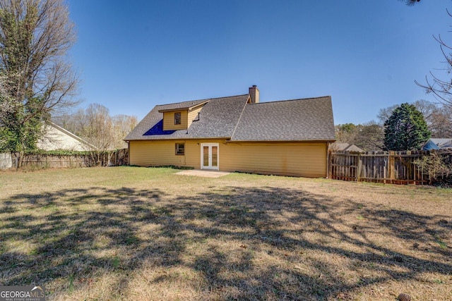 back of house featuring a fenced backyard, a yard, french doors, roof with shingles, and a chimney