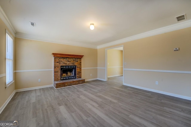 unfurnished living room featuring ornamental molding, a brick fireplace, visible vents, and wood finished floors