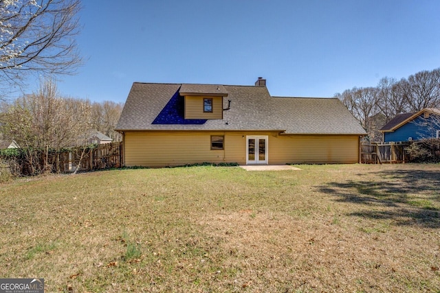 back of house featuring a shingled roof, a lawn, a fenced backyard, a chimney, and french doors