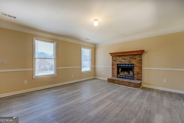 unfurnished living room with a brick fireplace, ornamental molding, and wood finished floors