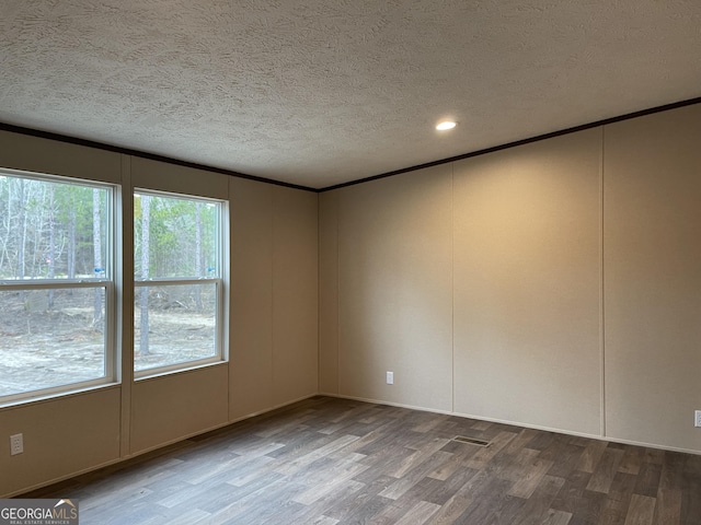 empty room with crown molding, a textured ceiling, a decorative wall, and wood finished floors