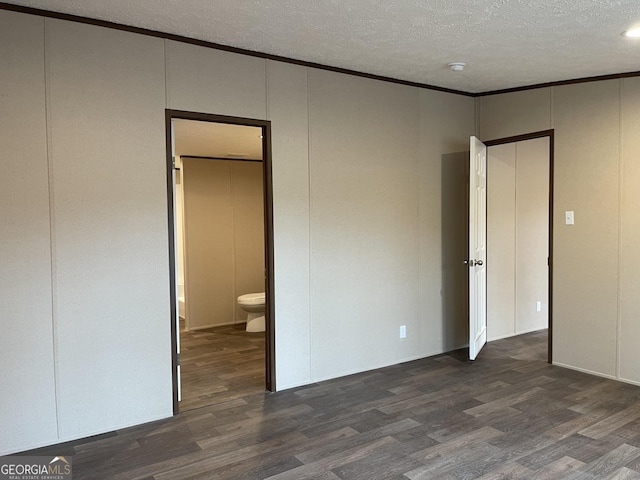 unfurnished bedroom with dark wood-style floors, crown molding, a decorative wall, and a textured ceiling