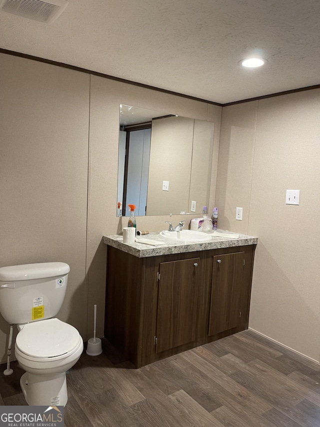 bathroom featuring a textured ceiling, toilet, wood finished floors, vanity, and visible vents