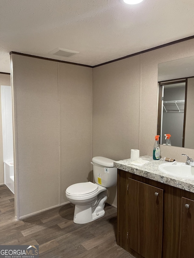 bathroom with a textured ceiling, toilet, wood finished floors, visible vents, and vanity