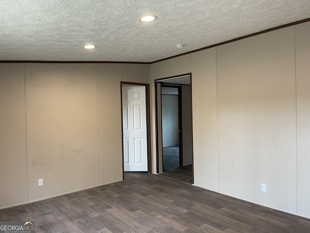 empty room with a textured ceiling, ornamental molding, a decorative wall, and dark wood-type flooring